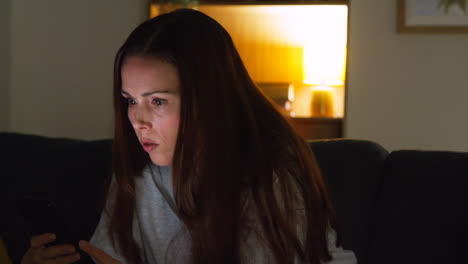 Anxious-Woman-Sitting-On-Sofa-At-Home-At-Night-Looking-At-Mobile-Phone-Concerned-About-Social-Media-Or-Bad-News-1